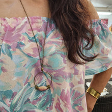 Load image into Gallery viewer, Person wearing a floral dress with a necklace, sitting on a floral-patterned surface.