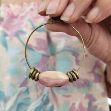 Load image into Gallery viewer, Hand holding a gold hoop pendant with pink bead against a colorful background
